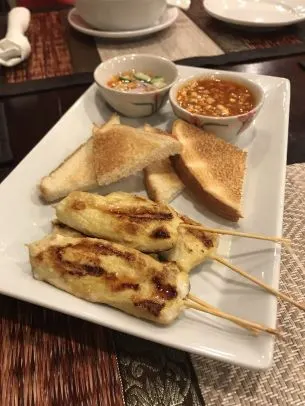 Gai Satay (Chicken Satay) — Chicken marinated in our special spices, skewered, grilled to perfection, and served with peanut sauce, cucumber salad, and toast.