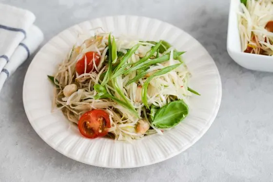 Som Tam (Papaya Salad) — Spicy green papaya salad with cherry tomatoes and green beans, topped with roasted peanuts.